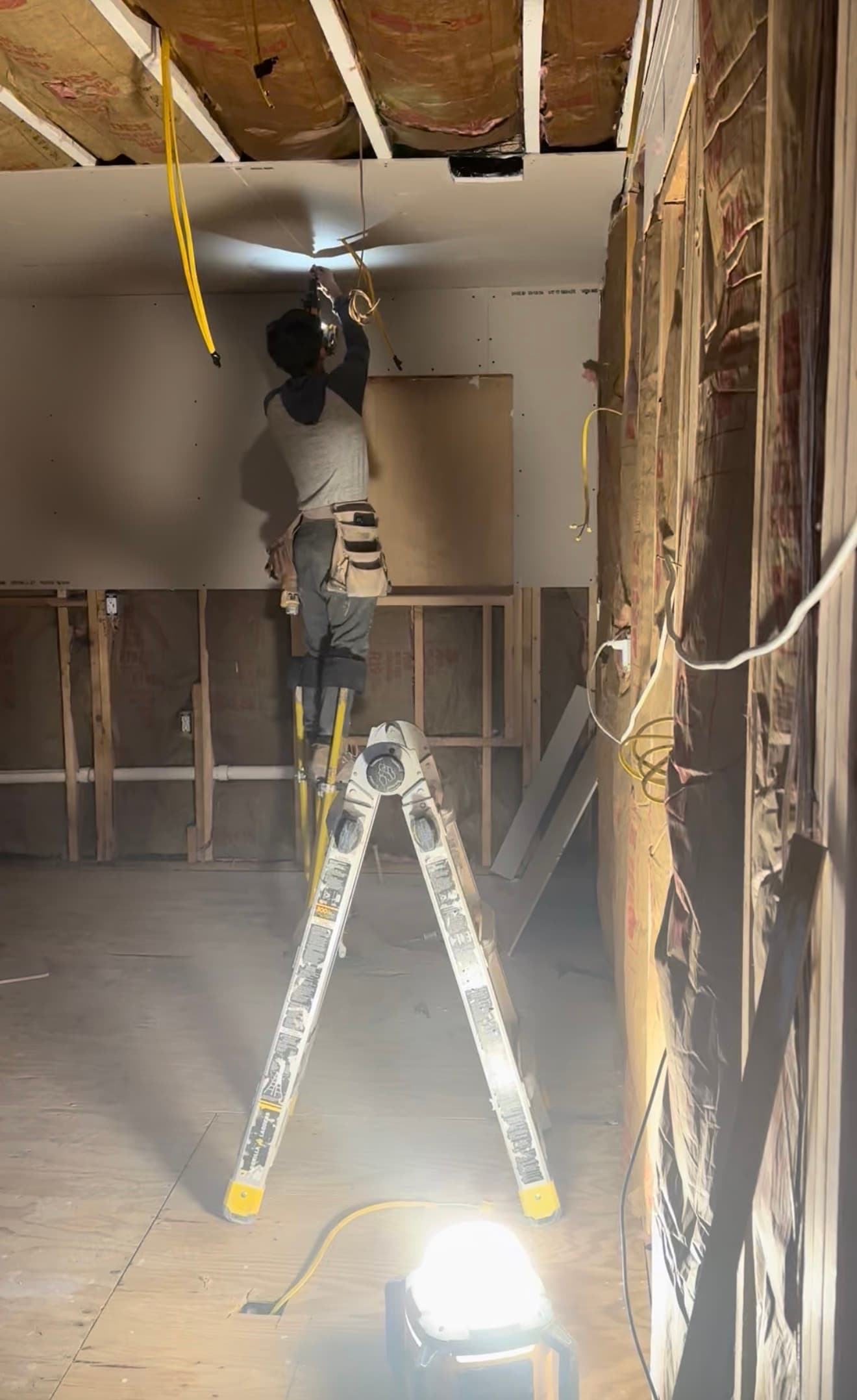 Construction worker on stilts installs drywall on a ceiling in a room under renovation.