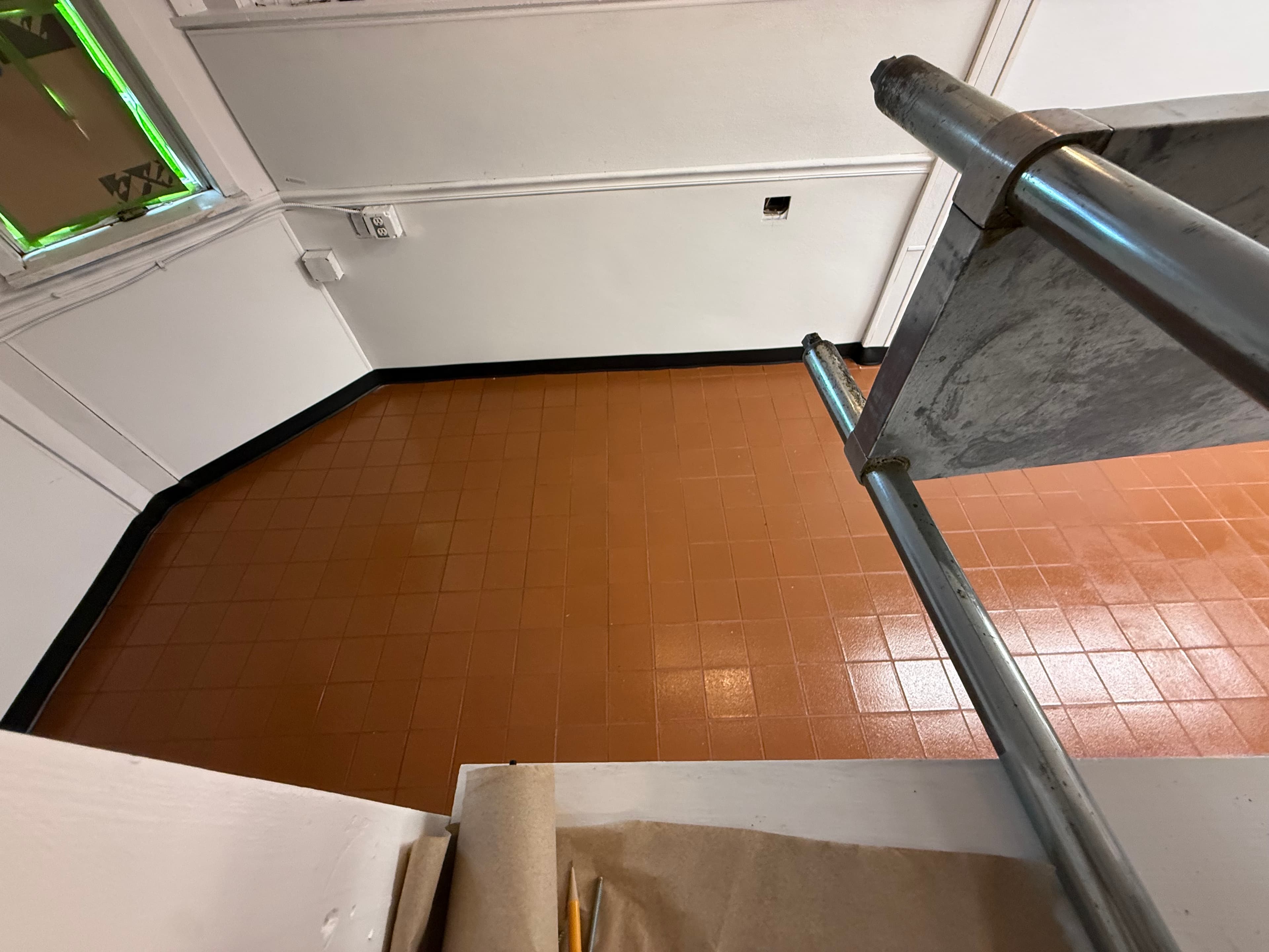 High-angle view of orange tiled floor and white walls from behind metal scaffolding pipes.