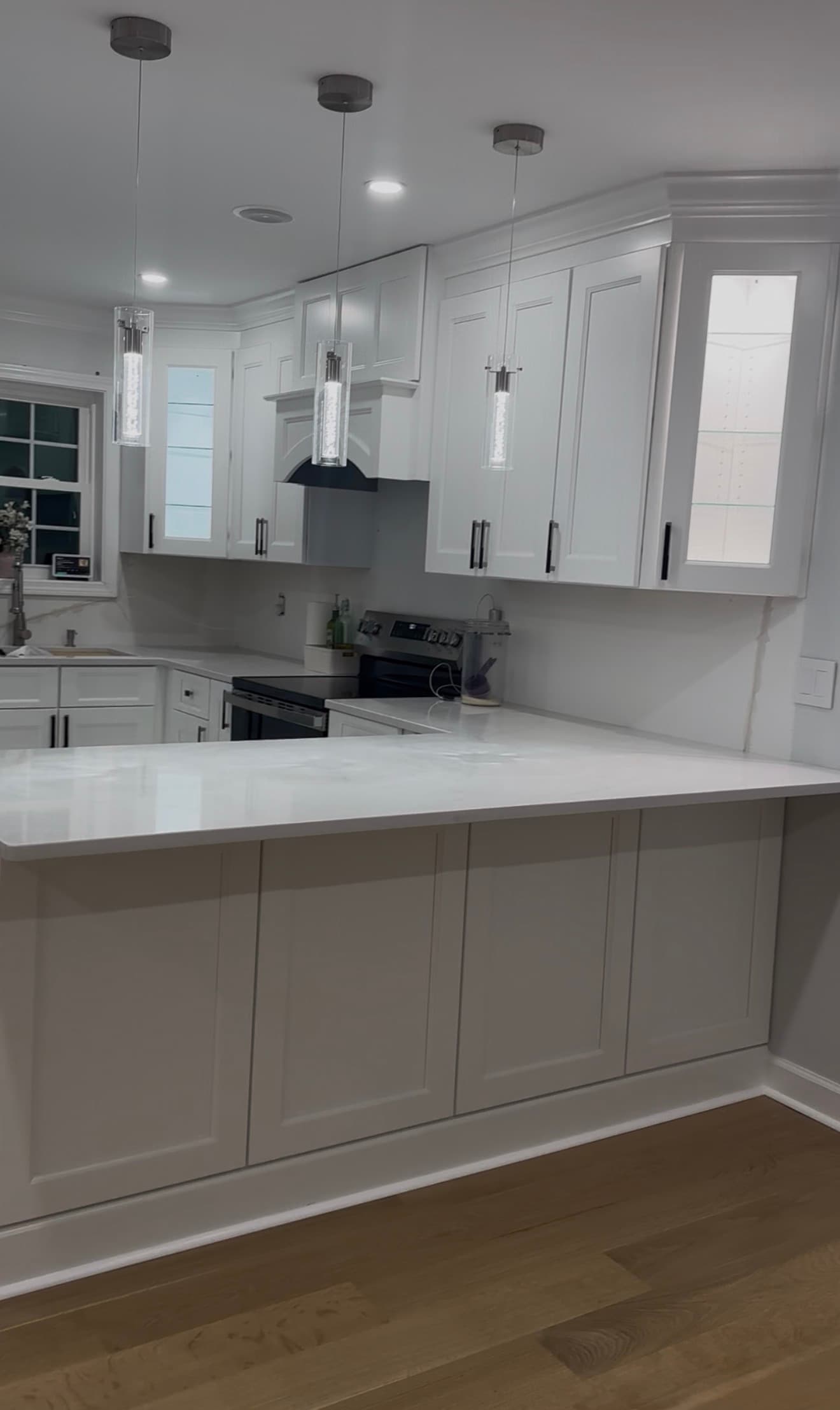 Modern white kitchen with shaker cabinets, quartz countertops, and three pendant lights over a peninsula.
